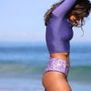 Person wearing a purple top and floral shorts on a beach