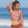 Woman wearing a floral long-sleeve top and brown bikini bottom on a beach.