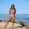 Woman in a floral bikini standing on a sandy beach with ocean in the background