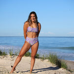 Woman in a floral bikini standing on a sandy beach with ocean in the background