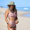 Woman in a floral bikini and bucket hat on a beach