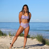Woman in a purple floral bikini standing on a sandy beach with ocean view