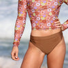 Person wearing a floral long-sleeve top and brown high-waisted bikini bottoms on a beach.