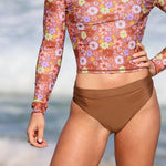 Person wearing a floral long-sleeve top and brown high-waisted bikini bottoms on a beach.