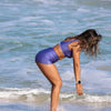 Woman in a purple swimsuit standing in the ocean water.