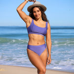 Woman in a purple bikini standing on a beach with ocean in the background
