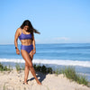 Woman in a purple bikini standing on a sandy beach with ocean in the background