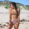 Woman in a bikini standing on a sandy beach with greenery in the background