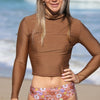 Woman wearing a brown long-sleeve top and floral shorts on a beach.
