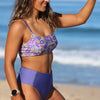 Woman wearing a purple floral bikini top and blue high-waisted bottoms on a beach.