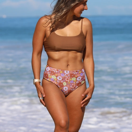Woman in a brown bikini top and floral patterned bottom standing on a beach.