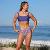 Woman in a purple bikini standing on a beach with ocean in the background