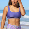Woman wearing a purple sports bra and floral shorts on a beach.