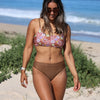 Woman in a floral bikini top and brown bottoms walking on a beach.