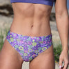 Purple floral bikini bottom worn by a person on a beach.