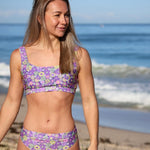 Woman wearing a purple floral bikini set on a beach