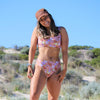 Woman in a floral bikini and cap standing in a desert-like landscape with clear blue sky.