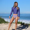 Woman in a purple swimsuit standing on a sandy beach with ocean in the background