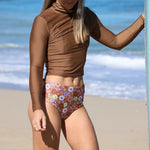 Person wearing a brown long-sleeve top and floral high-waisted bikini bottom on a beach.