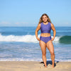 Woman in a purple swimsuit standing on a beach with ocean waves in the background