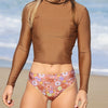 Person wearing a brown long-sleeve top and floral swimsuit on a beach.